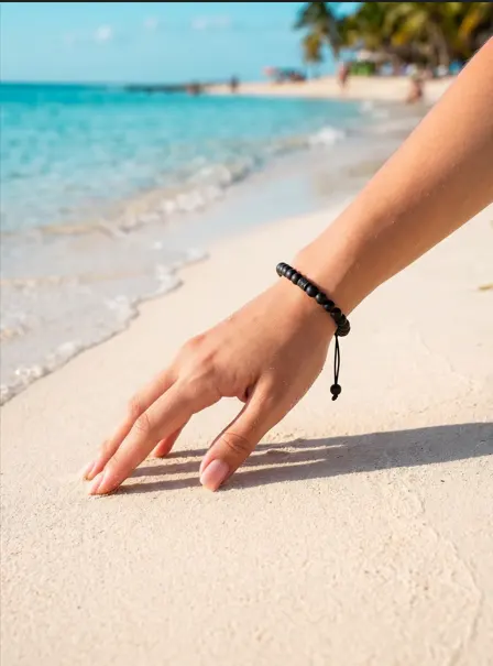 Pulsera artesanal de tapas recicladas en una muñeca, sobre la arena